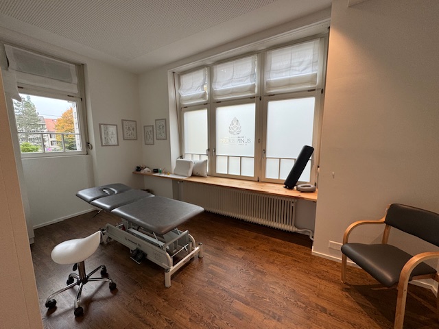 Zweiter Behandlungsraum mit höhenverstellbarer Therapieliege und grossflächigen Fenstern