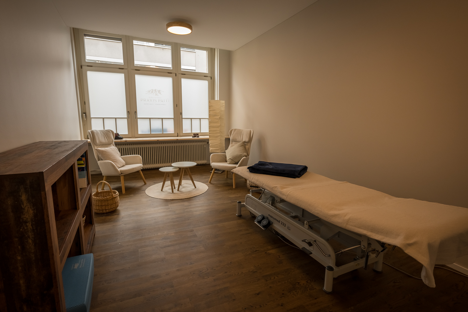 Heller Behandlungsraum der Praxis Pinus mit Therapieliege, zwei Sesseln und grossen Fenstern